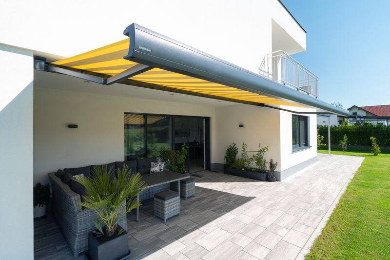 Lona toldo cofre MX-3 con tejido a rayas amarillas sobre una casa blanca.