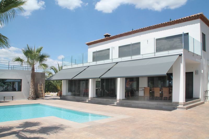 Reference image of cassette awning markilux 5010 in gray on white southern house with pool in the foreground.