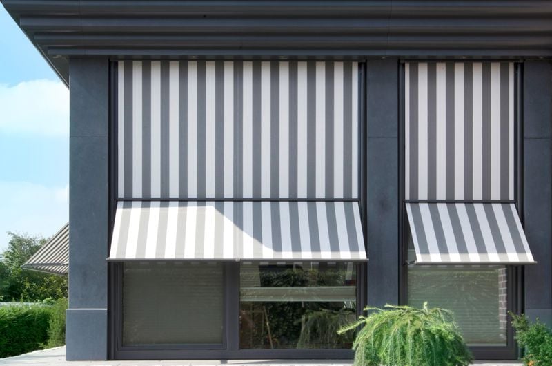 Referenzbild: Eckiger Anbau mit Fensterfronten ausgestattet mit Markisoletten markilux 740, grau-weiß gestreiftes Tuch.