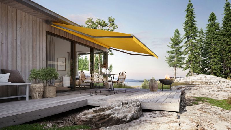 Folding arm awning markilux 930 in silver with yellow cloth on wooden house