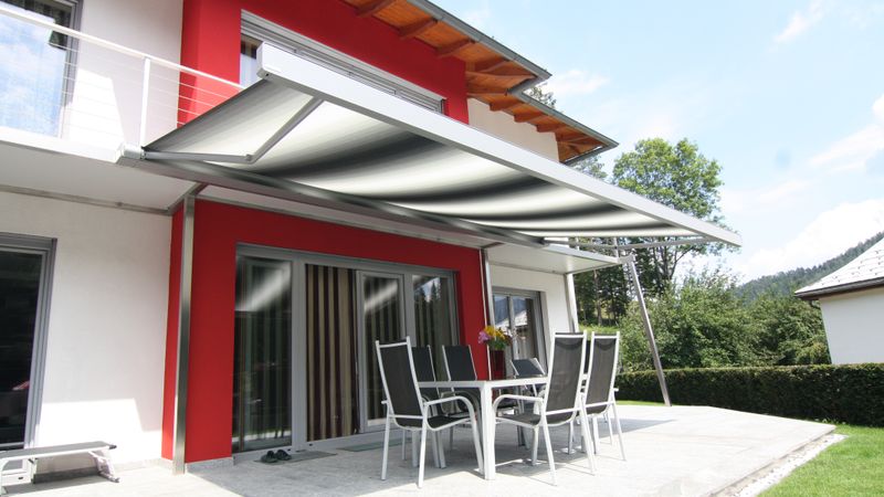 Tenda da sole a cassonetto markilux 970 a strisce grigio-bianche su casa intonacata di rosso