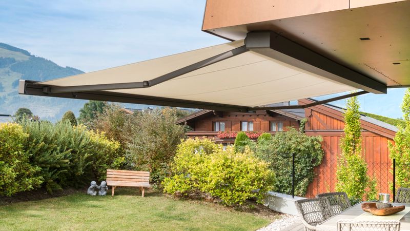 Cassette awning markilux 970 with beige cloth on covered terrace in front of alpine panorama