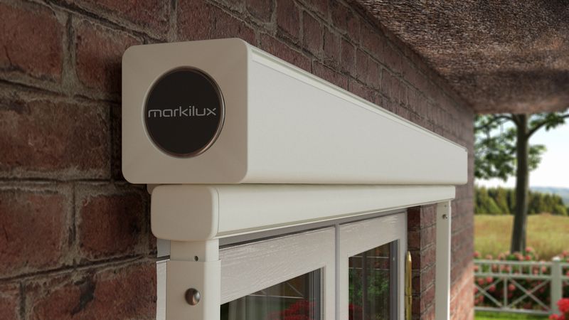 Detail view of drop-arm cassette awning markilux 730: white frame, retracted fabric cover, wall mounted.