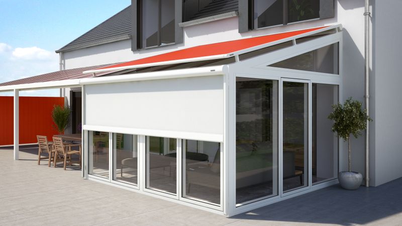 White house with orange on-glass awning markilux 870 on the adjacent conservatory. In addition, a vertical blind markilux 876 with white fabric cover is mounted on the side of the conservatory.
