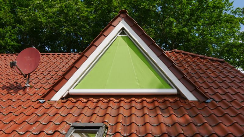 Dormer with triangular window and custom-fit vertical blaind awning markilux 893 with green fabric cover.