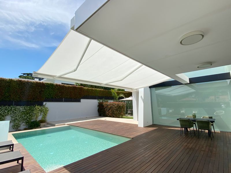 Store coffre blanc markilux 3300 sur une maison blanche avec terrasse en bois et piscine.