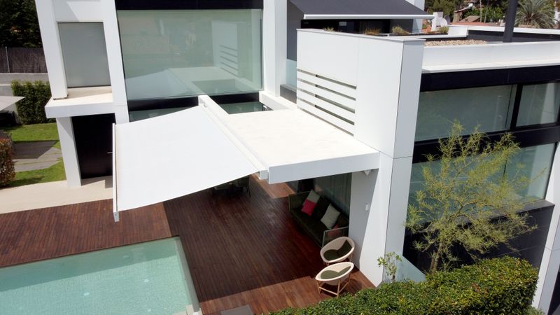 Toldo cofre blanco markilux 3300 sobre una casa blanca con terraza de madera y piscina.