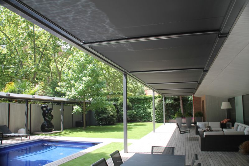 Covering of a hotel terrace by the top glass awning markilux 770 with black fabric cover next to the pool.