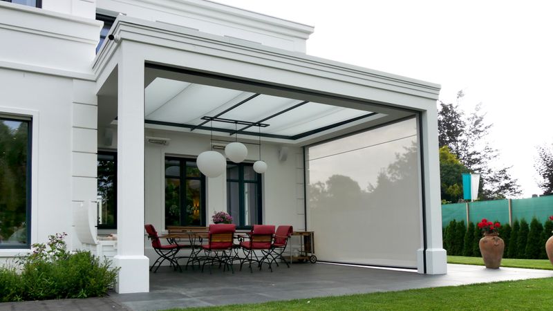 Chalet blanco con terraza cubierta equipada con toldo markilux bajo cristal y toldo vertical.