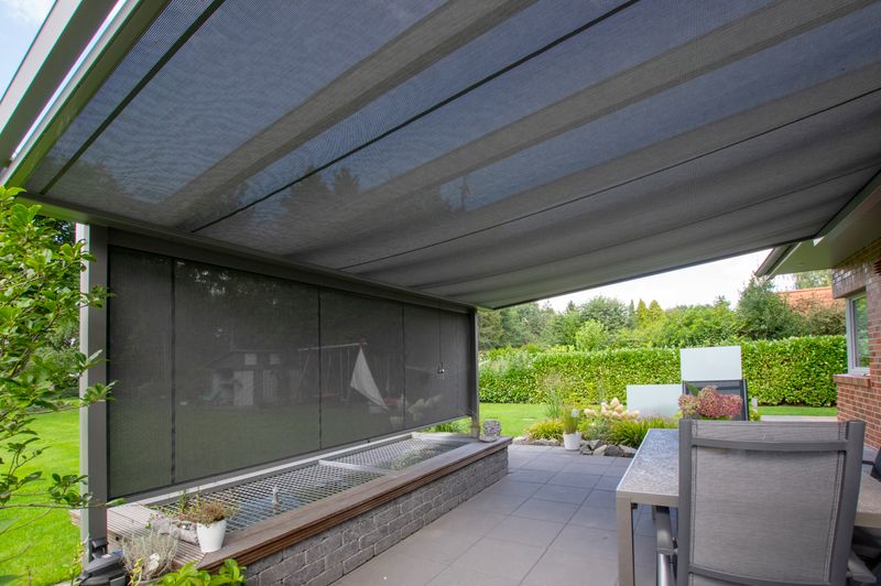 Seitliche Sicht unter ein Terrassendach mit markilux Unterglasmarkise mit transparentem Tuch, frontal ist zudem eine Vertikalmarkise angebracht.
