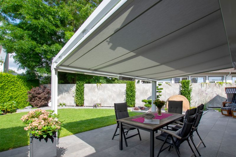 Copertura bianca per patio con tenda da sole per copertura in vetro markilux 779 con telaio bianco e tessuto della tenda da sole grigio.