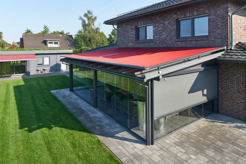 Conservatório com toldo markilux vermelho sobre vidro e estore vertical cinzento como protecção solar lateral.