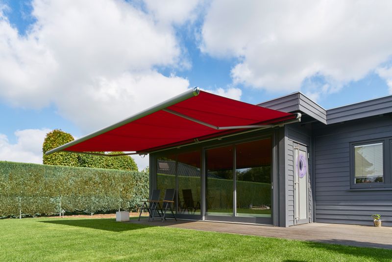 semi-cassette awning markilux 1600 with red fabric cover and gray frame in private garden.