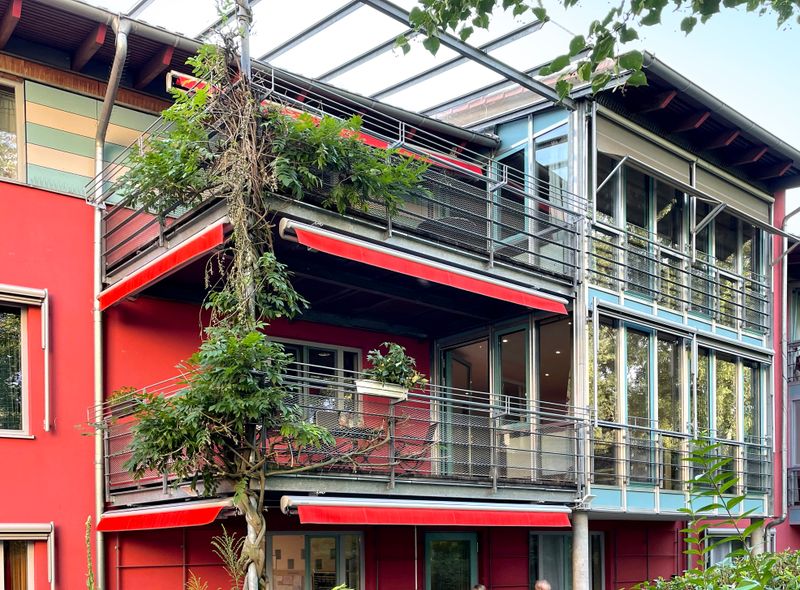 Flera indragna markiser markilux 1710 med rödrandigt tyg och valv på en röd byggnad för att skugga balkongerna.