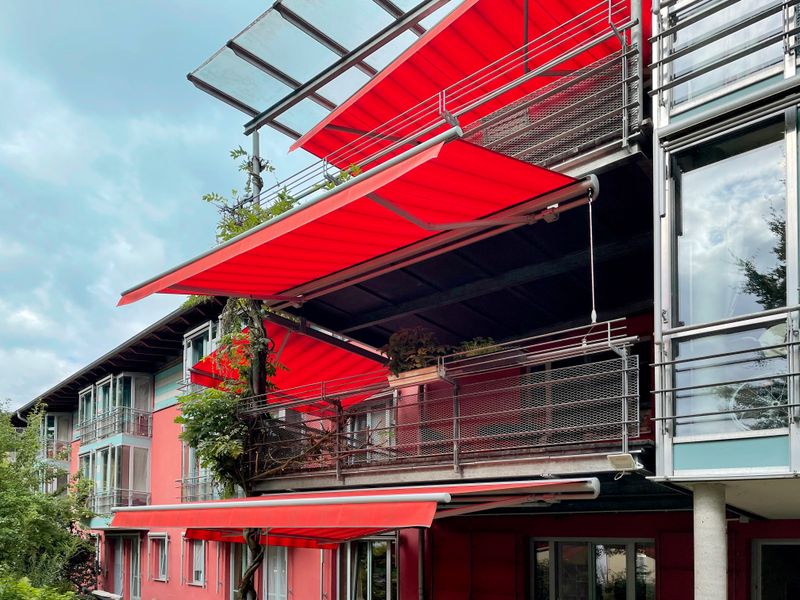 Several markilux 1710 with red striped fabric cover and valance on a red building to shade the balconies.