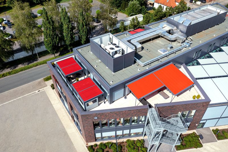 Image de référence de quatre stores avec toile de store rouge et armature anthracite sur la terrasse du toit du bâtiment markilux à Emsdetten.