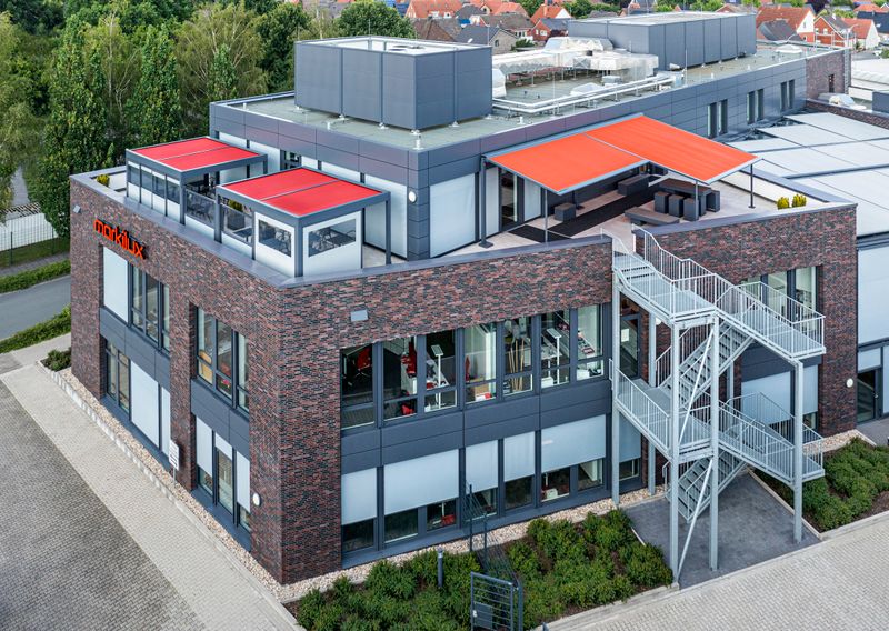 Photo de référence markilux pergola et markilux markant avec toile de store rouge et cadre anthracite sur le toit-terrasse du bâtiment markilux à Emsdetten.