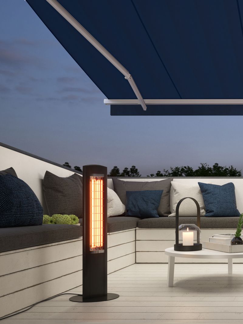 Open awning mx 1300 with silver frame and dark blue fabric cover rises above a terrace. There is a cozy evening atmosphere and a small heater is on the left side of the picture.