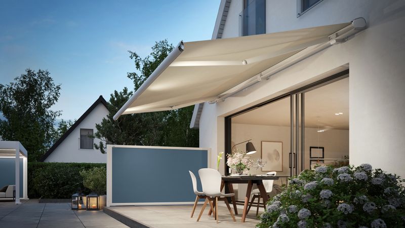 In the foreground of the terrace is the extended markilux 6000 with cream-colored frame and fabric cover. It looks like a summer evening atmosphere.