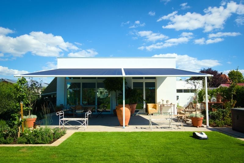référence markilux pergola classic, toile de store bleue, maison blanche. protection solaire pour terrasse dans le jardin.