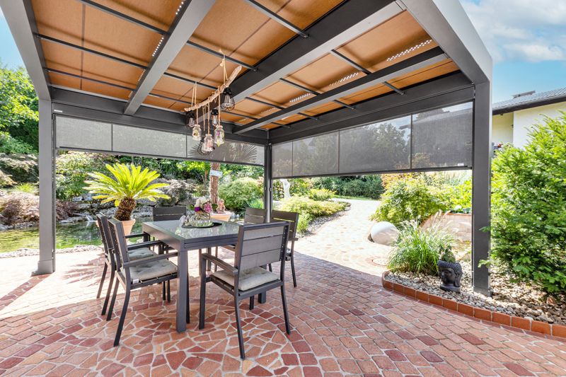 Reference of a freestanding patio cover markilux markant with beige awning cover and vertical blind with gray translucent awning cover, on a Mediterranean terrace away from the house.
