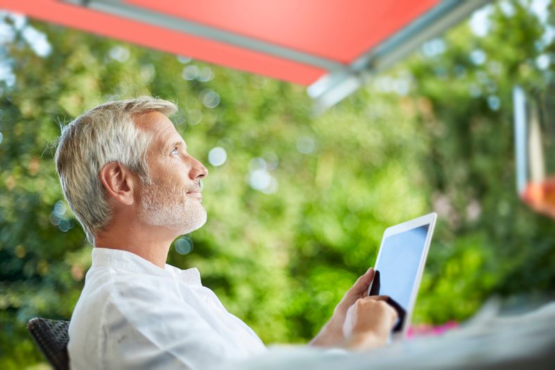 Man sits under awning and controls it with an iPad.