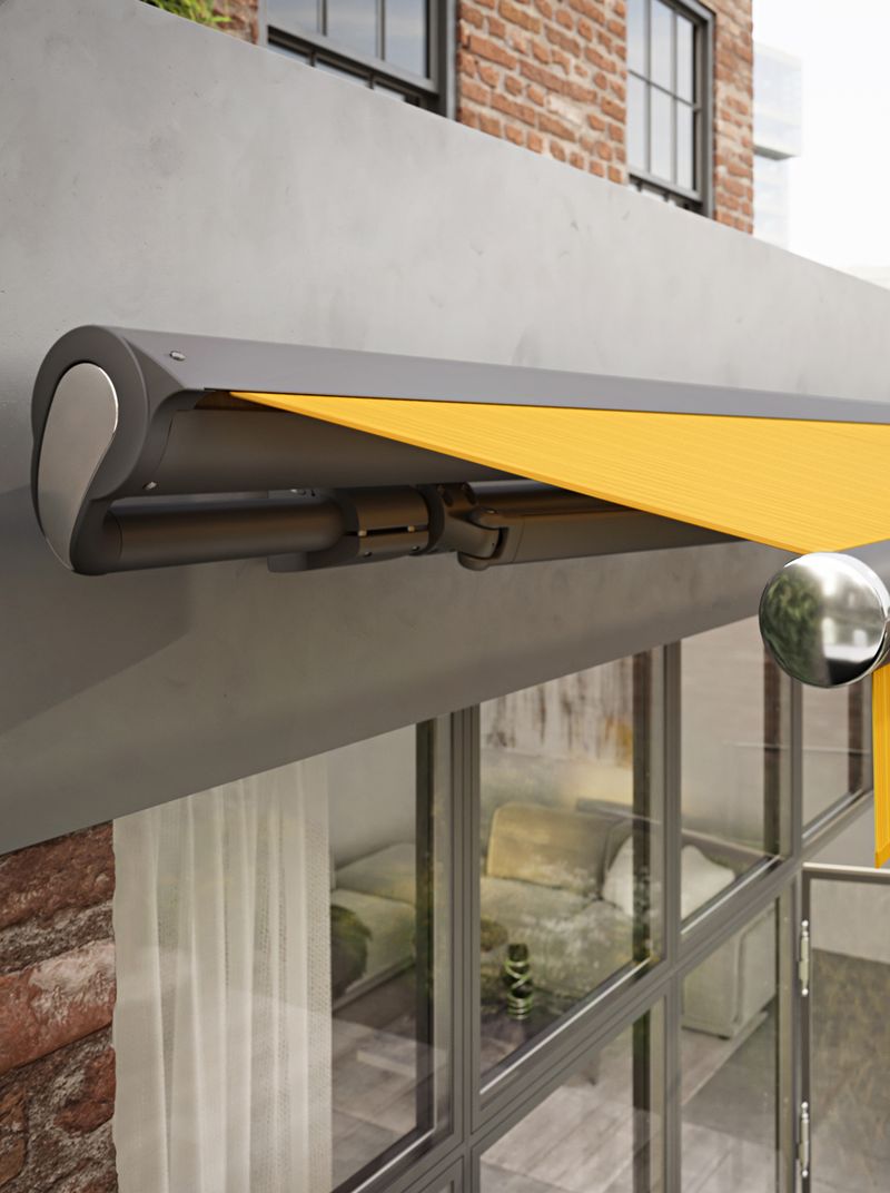 Cassette awning markilux 1710 with a yellow striped fabric cover, a dark gray frame and chrome end caps. The awning is attached to a factory loft.