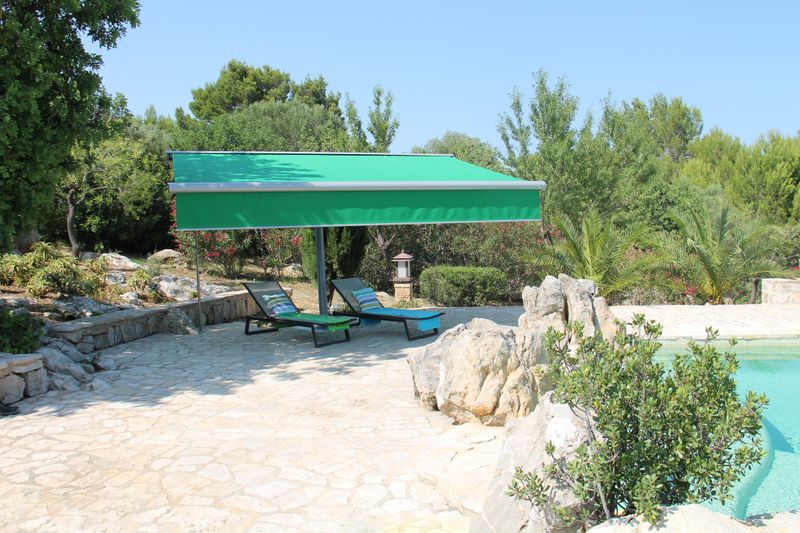 Entoilage parasol markilux planet avec toile de store verte et shadeplus au bord d'une piscine méditerranéenne avec transats et palmiers.