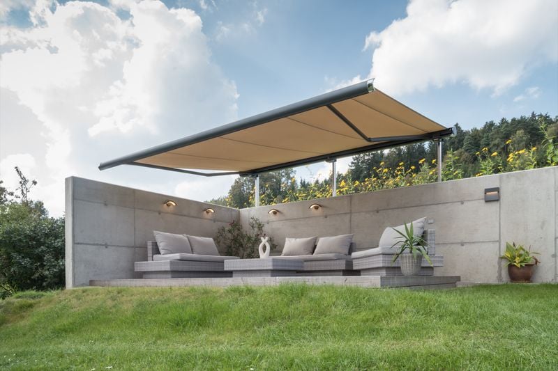 Reference image: cassette awning markilux 6000 (frame anthracite, fabric cover beige) attached to stand system for shading a seating area on a lawn.