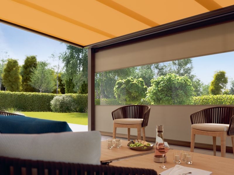 Cubierta de terraza con zona de asientos protegida del viento por un toldo vertical tipo markilux 776/876 con ventana panorámica.