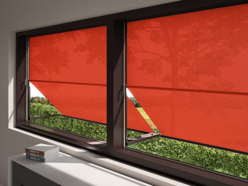 Ansicht von drinnen nach draußen. Die Fenster sind mit einer Markisolette markilux 740 mit rotem, transparenten Tuch ausgestattet.