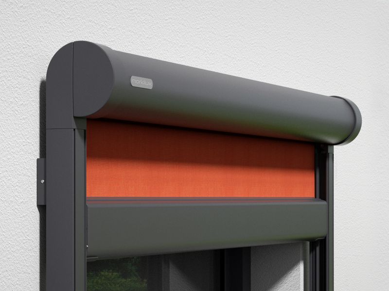 Detaljvy av vertikal kassettmarkis markilux 876: grå ram, orange tygduk, väggmonterad.