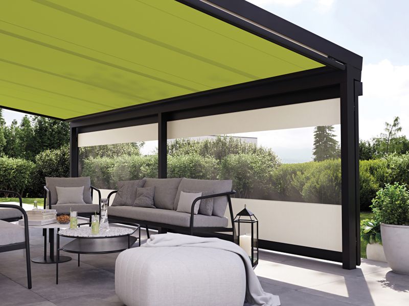 Sala de estar ao ar livre coberta com toldo de lona de vidro markilux 779 com cobertura de tecido verde brilhante, complementada por uma persiana vertical com janela panorâmica.