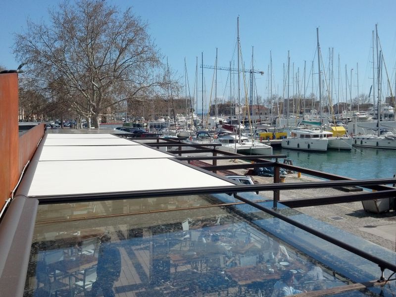 Restaurangterrass vid hamnen täckt med terrasstak och markis Markilux 8800 med vit tygduk