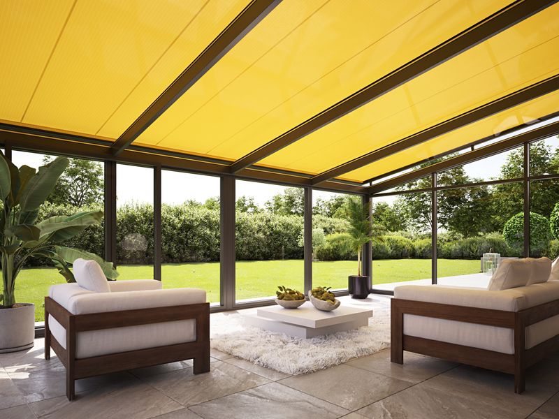 Interior view of a conservatory overlooking the lawn of the garden. Conservatory awning with yellow fabric cover shades the seating area.
