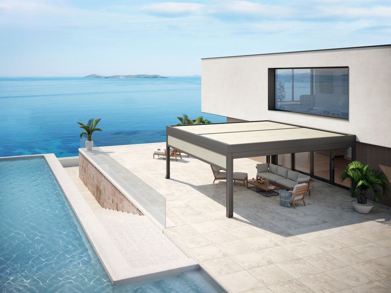 Maison blanche au bord de la mer et terrasse avec piscine. Système de store markilux markant comme protection solaire pour le coin salon.