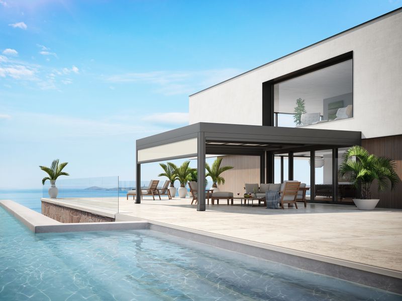 Casa blanca junto al mar y terraza con piscina. Sistema de toldo markilux markant como protección solar para la zona de estar.