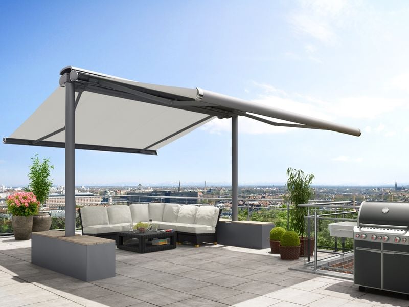 Awning stand system markilux syncra with white awning cover and gray frame, fixed with stabilisation boxes on a roof terrace overlooking the city.
