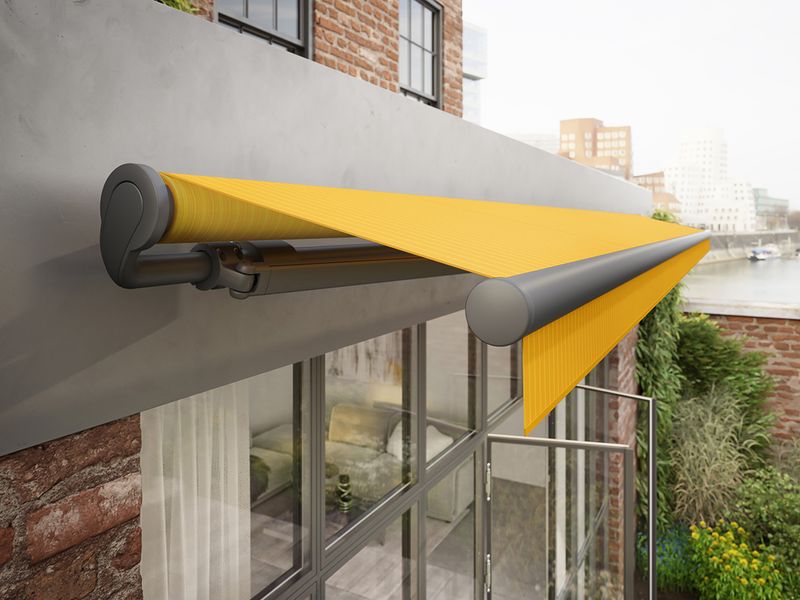 Open folding-arm awning markilux 1700 with yellow fabric cover attached to the wall of a factory loft.