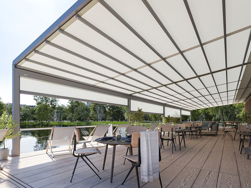 Terraza de restaurante junto al lago, cubierta con una markilux pergola stretch con marco gris y tejido blanco. Completada con estores verticales blancos.