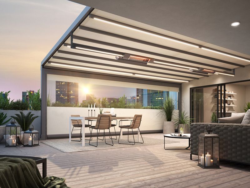 Penthouse terrace in a big city at sunset. The seating area of the roof terrace is covered with a markilux pergola stretch, equipped with infrared heaters and LED-Line, gray frame, white fabric cover. A vertical blind with panoramic window serves as a lateral windbreak, providing a view of the skyscrapers.