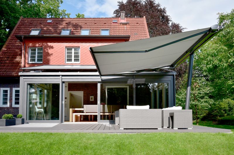 Awning parasol markilux planet with a cassette awning markilux 5010 with light fabric cover provides shade over a seating area on the terrace of a family house.