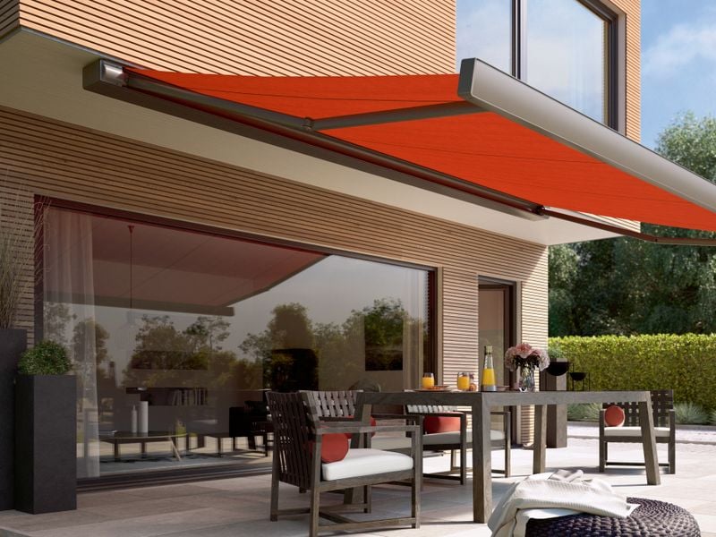 Kassettenmarkise markilux 970 mit rotem Tuch, angebracht unter dem Dachvorstand eines Holzhauses als Sonnenschutz für die Terrasse.