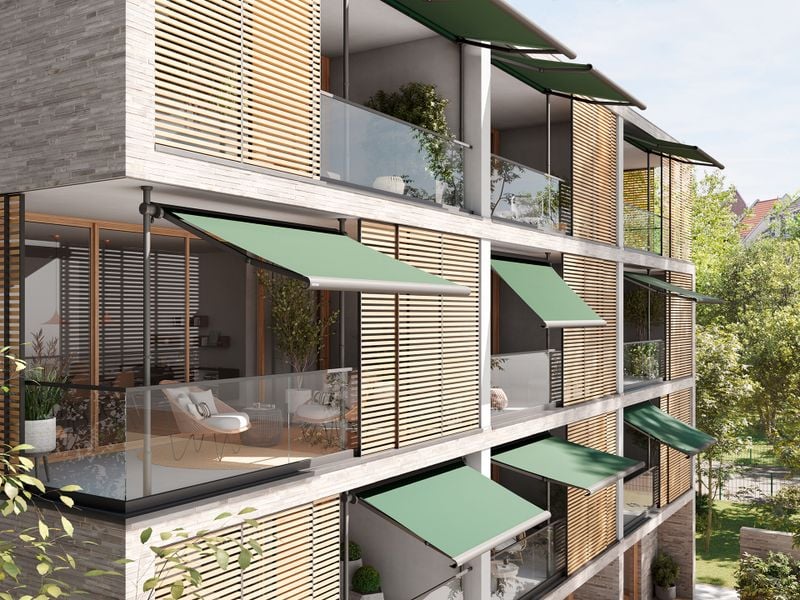 Seitenansicht eines modernen Mehrfamilienhaus mit mehreren Balkonen, die jeweils mit einer markilux 900 Klemmmarkise ausgestattet sind. Die Markisen sind optisch einheitlich mit grünem Tuch ausgestattet. Der Neigungswinkel der Markise unterscheidet sich je nach Balkon.