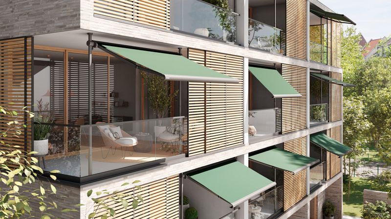 Seitenansicht eines modernen Mehrfamilienhaus mit mehreren Balkonen, die jeweils mit einer markilux 900 Klemmmarkise ausgestattet sind. Die Markisen sind optisch einheitlich mit grünem Tuch ausgestattet. Der Neigungswinkel der Markise unterscheidet sich je nach Balkon.
