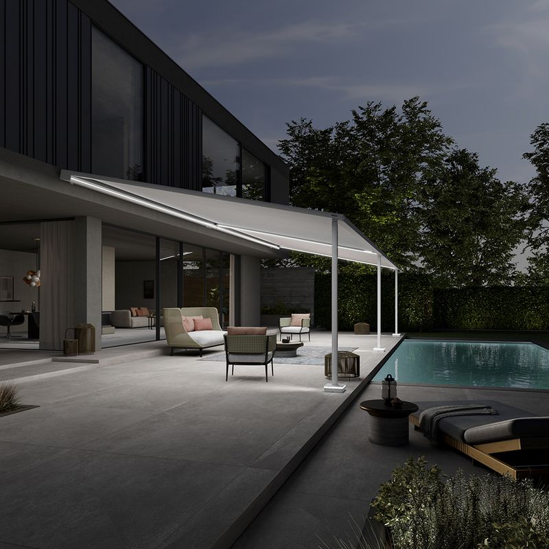 Pergolamarkise markilux style an einem modernen, schicken Kubusgebäude. Die Beleuchtung der Pergola taucht die Terrasse und den Garten mit Pool in schönes Licht.