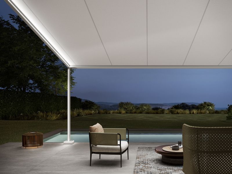 View below a white markilux pergola style with a view of the spacious garden with pool adjacent to the terrace. LED-Lines are integrated into the guide tracks, support posts and feet of the pergola.