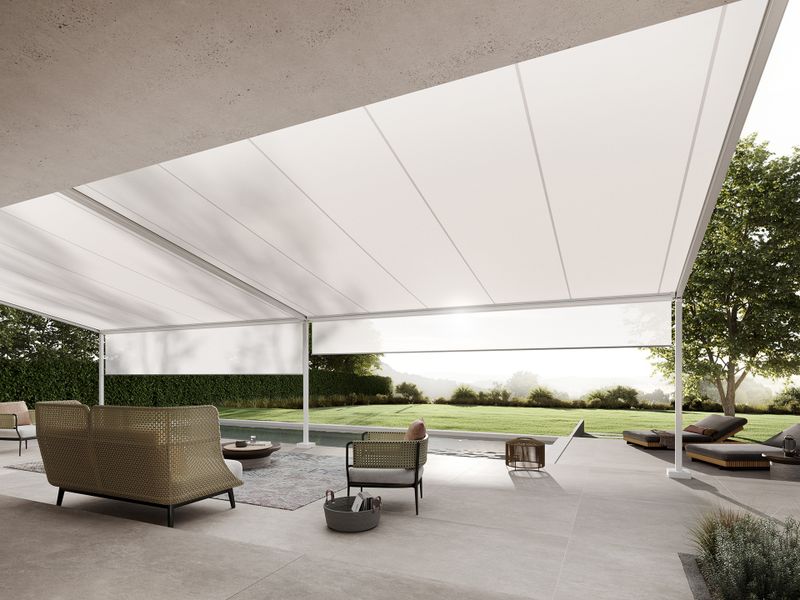View below a white markilux pergola style with a view of the spacious garden with pool adjacent to the terrace. Shadeplus is integrated into the front profile of the pergola to protect against low sun.