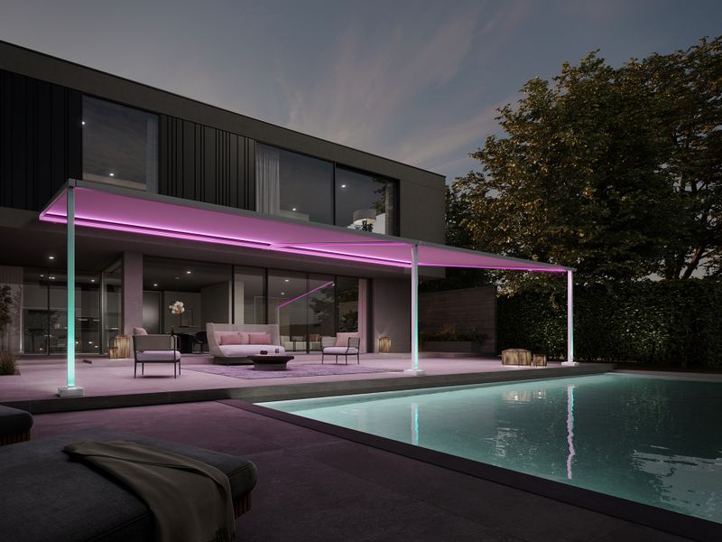 Pergolamarkise i Markilux-stil på en moderne, elegant kube-bygning. Pergolaens lyserøde belysning bader terrassen og haven med pool i smukt lys.