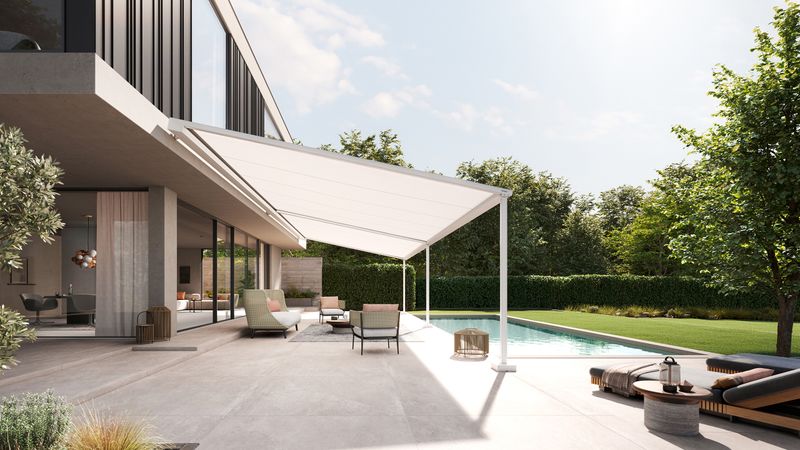 Side view of a modern cube building made of concrete and wooden elements. A markilux pergola style pergola awning with white awning cover covers the terrace right up to the adjacent pool.